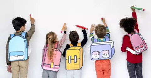 enfant en train d'écrire le long d'un mur blanc avec des sacs dessinés pour la garderie - inscriptions scolaires