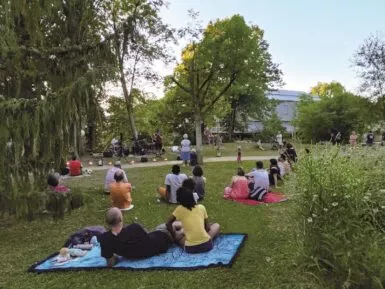 photo prise à l'occasion des mardis musicaux sur l'île verte. en premier plan des gens sont assis sur une serviette, ils regardent un concert
