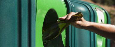une main met une bouteille dans un container à verre
