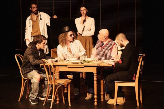 La maladie de la famille M (Collectif Nuit Orange) 6 comédiens sont sur scène, 4 sont assis à une table et les 2 autres les observent, debout